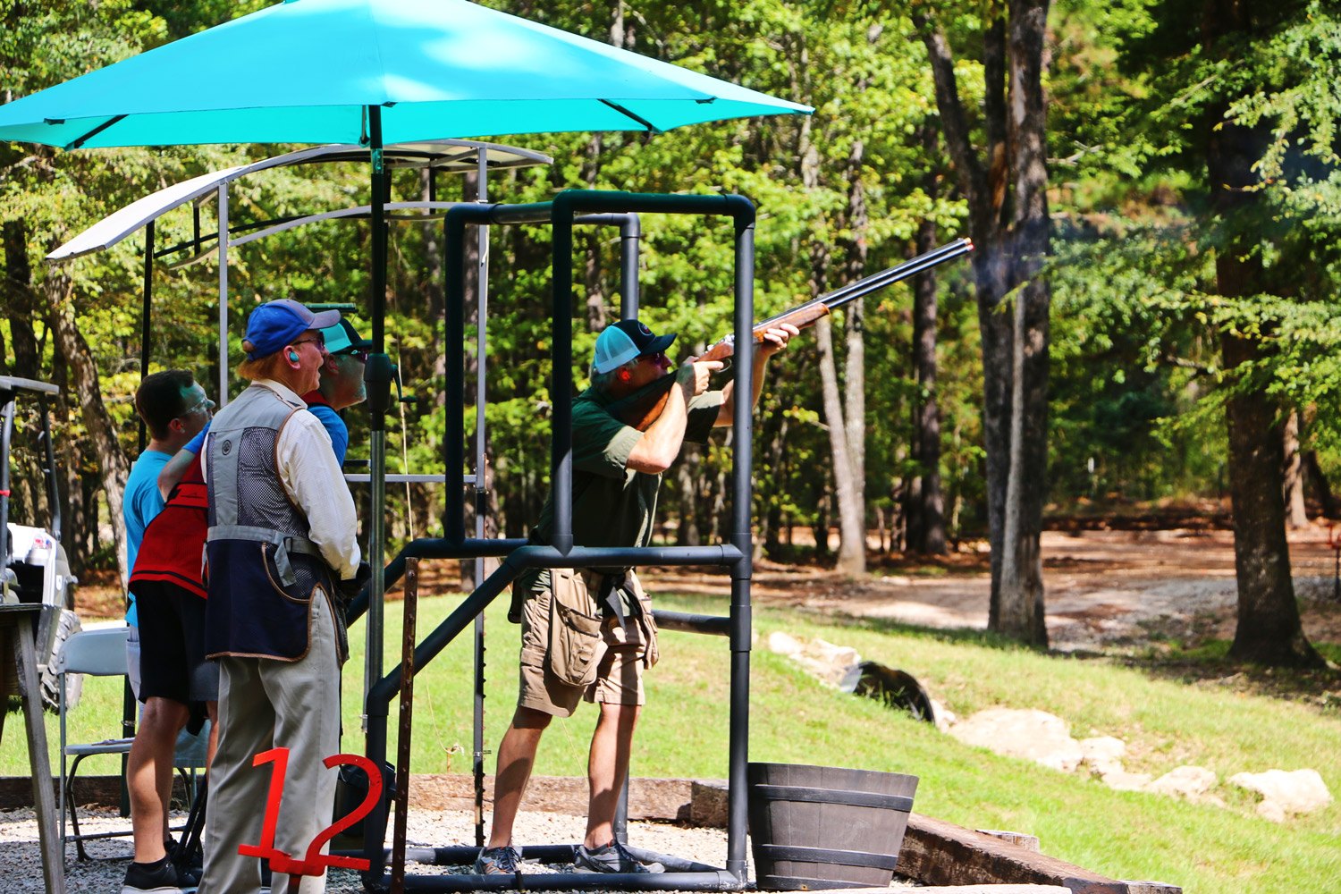 A shooter fires at a station on the sporting clay course while others watch
